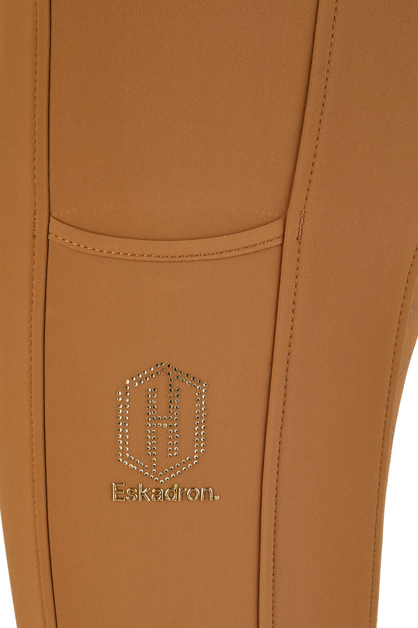 Gros plan sur un pantalon de couleur camel avec une poche. Le logo incrusté de strass de la marque "Eskadron" est visible sous la poche.