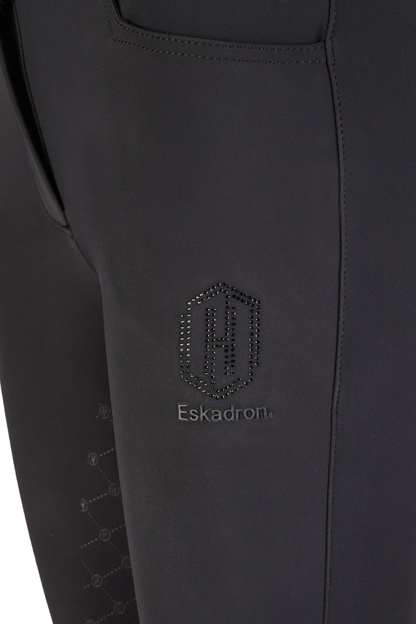 Close-up sur la cuisse d'un pantalon d'équitation noir avec le logo "Eskadron" brodé et des détails incrustés de petits cristaux formant un motif géométrique.