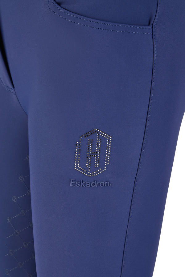 Alt : "Gros plan sur une pièce de vêtement bleu avec un logo hexagonal en strass et la marque 'Eskadron' brodée en dessous."