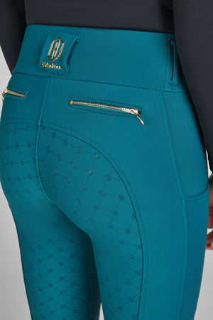 "Vue rapprochée d'un pantalon d'équitation teal avec détails de motifs géométriques sur l'arrière. Le pantalon comporte des poches zippées dorées et un logo métallique doré de la marque "Eskadron" cousu à la taille."