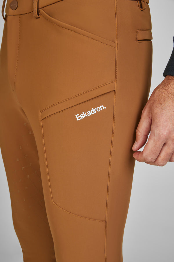 "Vue rapprochée d'un pantalon d'équitation marron avec une poche sur le côté, marqué du logo 'Eskadron'. Une main est visible à droite de l'image."