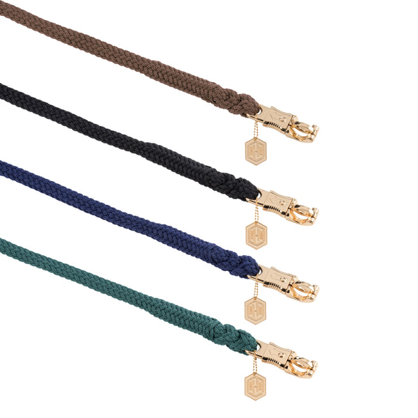 Quatre laisses tressées de différentes couleurs (marron, noir, bleu marine et vert), chacune équipée d'un mousqueton en métal doré avec un médaillon hexagonal doré attaché.