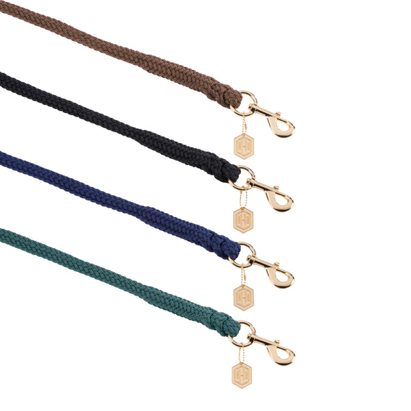 Quatre laisses en corde tressée de différentes couleurs (marron, noir, bleu et vert) disposées en parallèle. Chaque laisse est équipée d'un mousqueton doré avec un pendentif hexagonal portant un logo gravé.