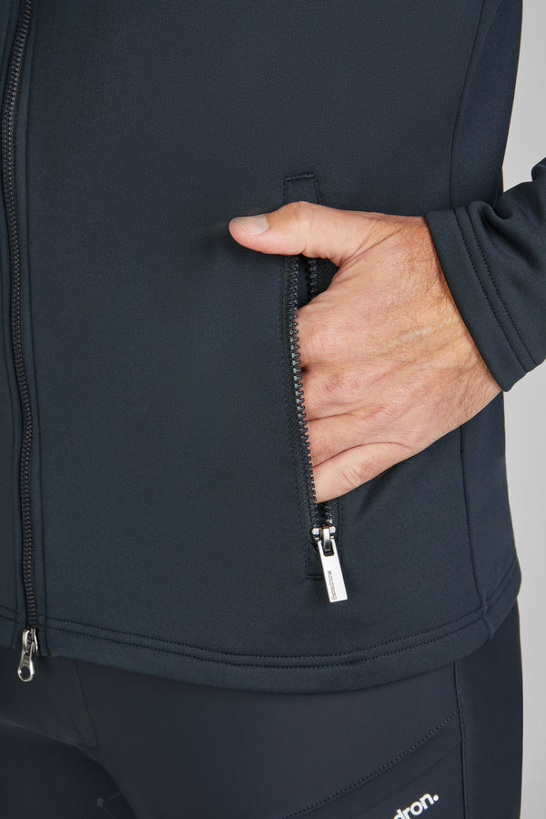 Main d'une personne zippant la poche d'une veste noire, près du bas de celle-ci. Une partie du bras et du bas de la veste est visible, ainsi que le logo "Eskadron" sur le bas du pantalon noir.