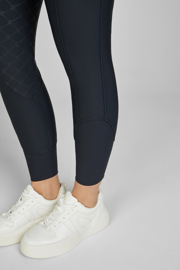 Personne portant un legging noir ajusté avec des détails imprimés sur une jambe, associé à des baskets blanches. Seules les jambes et les chaussures sont visibles.