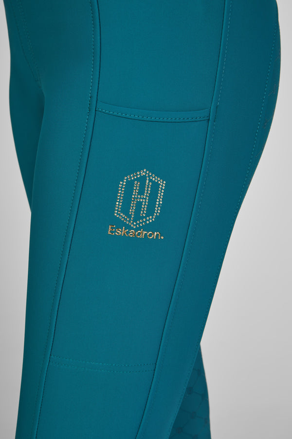 Pantalon d'équitation bleu turquoise avec une poche latérale et le logo doré de la marque Eskadron orné de petits cristaux.