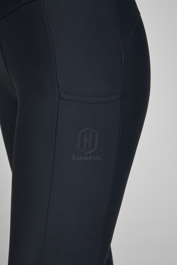 Close-up de la jambe d'un pantalon d'équitation noir portant le logo de la marque Eskadron, visible sur la cuisse.