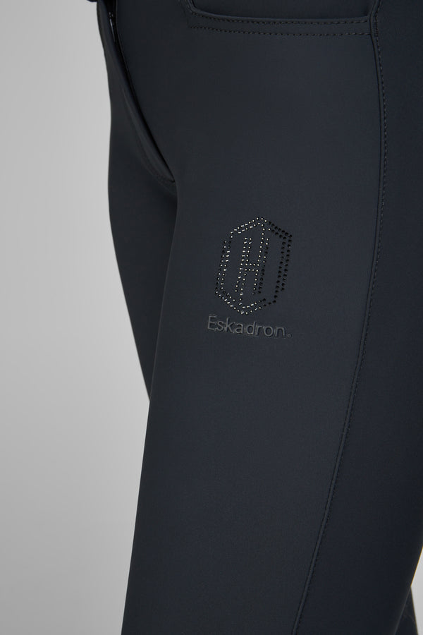 Pantalon de sport noir composé de tissu stretch, comportant une fermeture éclair sur le côté de la taille et un logo "Eskadron" en relief incrusté de petits points brillants.