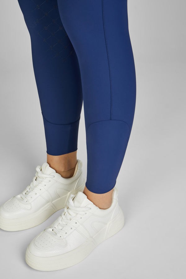 "Personne portant des leggings ajustés bleu marine et des baskets blanches épaisses sur un fond neutre."