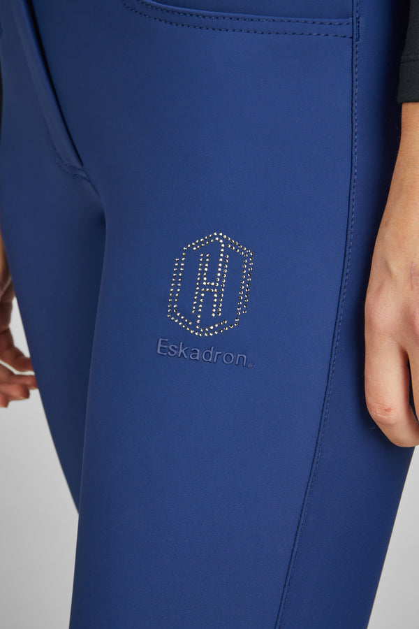 Gros plan d'une personne portant un legging bleu avec le logo "Eskadron" et un motif brillant en forme d'hexagone, situé sur le haut de la cuisse.