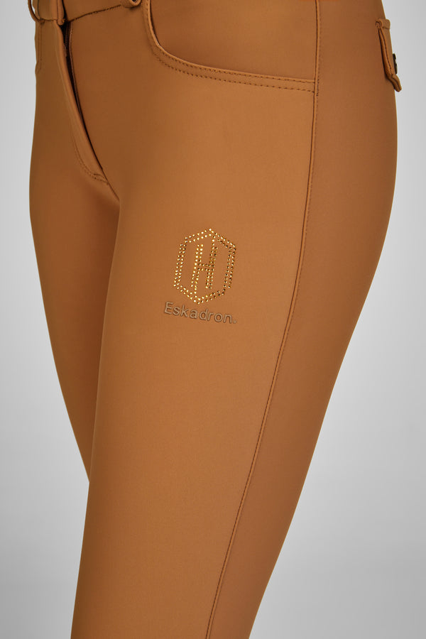 Alt : "Gros plan sur la partie supérieure de pantalon d'équitation marron avec logo 'Eskadron' et dessin incrusté de petits cristaux dorés sur la jambe."