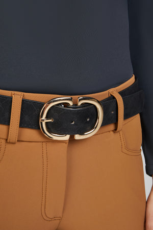 Ceinture en cuir noir avec une boucle dorée et un motif discret portée avec un pantalon camel.