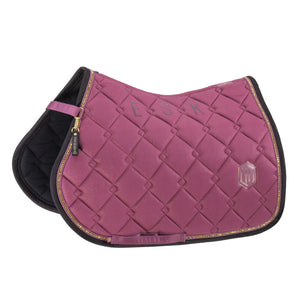 L'image montre une selle d'équitation de couleur bordeaux. La selle est conçue avec un motif matelassé en losanges, offrant une texture sophistiquée et confortable. Elle est bordée d'une fine ligne dorée qui ajoute une touche d'élégance et de raffinement. Sur le côté droit de la selle, il y a un logo en forme d'hexagone avec les lettres "HK" inscrites à l'intérieur. Ce logo semble être une marque ou un emblème de qualité. À gauche, trois lettres "A", "S" et "K" sont brodées en gris sur le...