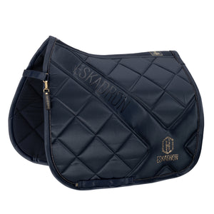 L'image présente une tapis de selle conçu pour l'équitation, qui est de couleur bleu nuit. Le tapis de selle est orné de motifs en losanges matelassés, lui donnant un aspect élégant et sophistiqué. En haut du tapis, le mot "ESKADRON" est brodé en grandes lettres dorées, ajoutant une touche de luxe à l'ensemble. Sur le côté droit, un logo composé d'un "H" stylisé et des lettres "ESKADRON" est également brodé en doré, renforçant l'identité de la marque. Le tapis de selle possède des sangles...