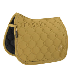 L'image montre une selle d'équitation de couleur moutarde. La selle est conçue avec un motif matelassé en losanges, offrant un aspect texturé et élégant. Sur le côté gauche de la selle, il y a une bande noire avec des éléments dorés, y compris une petite étiquette ou un logo. La partie supérieure de la selle est ornée des lettres "ESK" en doré, probablement pour personnaliser la selle avec des initiales. Le bord de la selle est fini avec une bordure dorée, ajoutant une touche de...
