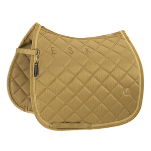 L'image représente une selle d'équitation de couleur dorée, soigneusement conçue avec un motif de losanges matelassés. La selle est ornée de lettres "ESK" brodées au centre, probablement des initiales personnalisées. Elle est équipée de finitions élégantes, notamment une bordure dorée qui ajoute une touche de sophistication. Sur le côté gauche de la selle, un étrier en métal doré est fixé, avec une petite étiquette pendante où l’on peut lire "ESK - Equestrian Stockholm". Cette étiquette...