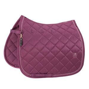 L'image montre une selle d'équitation de couleur bordeaux. La selle est conçue avec un motif matelassé en losanges, offrant un aspect texturé et élégant. Les bords de la selle sont ornés d'une fine bordure brillante, ajoutant une touche de sophistication. Sur la partie supérieure de la selle, les lettres "ESK" sont brodées en bordeaux, se fondant harmonieusement avec la couleur de la selle. À gauche de la selle, il y a une sangle de fixation, également en bordeaux, qui est attachée par une...