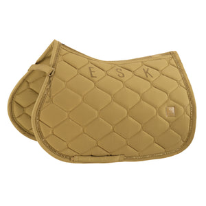 L'image montre un tapis de selle pour cheval de couleur beige clair. Ce tapis de selle est conçu avec un motif de losanges cousus, créant une apparence matelassée et texturée. Le bord du tapis de selle est orné d'une fine bande dorée, ajoutant une touche d'élégance à l'ensemble. Sur le côté droit du tapis, il y a un petit logo carré avec une bordure dorée, probablement indiquant la marque du produit. Les lettres "ESK" sont brodées de manière proéminente sur la partie supérieure du tapis de...