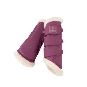 L'image montre une paire de protège-boue pour chevaux, de couleur bordeaux, avec des finitions en fourrure blanche sur les bords inférieurs et supérieurs. Les protège-boue sont conçus avec trois sangles ajustables dotées de boucles, permettant de les fixer solidement aux jambes du cheval. Sur le devant de chaque protège-boue, il y a un logo en relief représentant un "H" stylisé, accompagné des mots "ESKADRON EQUIPEMENT". Le logo est doré et rose, ajoutant une touche élégante et distinguée à...
