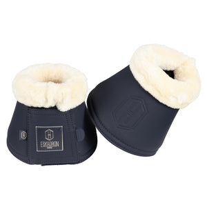 L'image montre une paire de bottes d'équitation de la marque ESKADRON. Elles sont conçues pour protéger les jambes du cheval, plus précisément la partie inférieure entre le genou et le sabot, souvent appelées guêtres ou bottes de protection. - **Matériaux et Design**: - Les bottes sont fabriquées en cuir ou en un matériau similaire, de couleur bleu foncé. - La partie supérieure des bottes est garnie d'une doublure en fourrure blanche, probablement en fausse fourrure, pour un confort et...