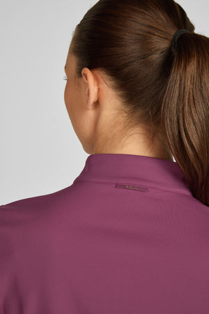 Cette image montre une femme vue de dos, portant un polo de couleur violet foncé. La personne a les cheveux longs attachés en queue de cheval haute et soignée. Le polo semble être bien ajusté et est doté d'un petit logo ou étiquette au niveau de la nuque, près du col. La texture du tissu semble être légèrement gaufrée, donnant un aspect soigneusement structuré. Le col est fermé et semble avoir une forme classique et ajustée. L'éclairage est neutre, mettant en évidence les détails du vêtement...