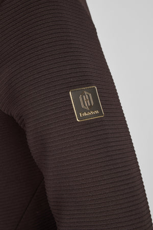 L'image montre un vêtement en tissu à maille côtelée de couleur marron foncé, probablement une manche, avec un logo brodé en or. Le logo est rectangulaire et comprend une partie visuelle et textuelle. La partie visuelle du logo représente un motif stylisé de trois lignes verticales se croisant en leur centre. En dessous de ce motif, le texte "Eskadron" est brodé en lettres capitales dorées. Le tissu semble souple et extensible, ce qui suggère qu'il pourrait s'agir d'un vêtement confortable,...