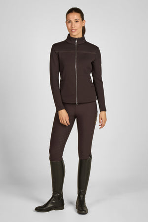 Dans l'image, on voit une femme debout devant un fond blanc uni, ce qui met en valeur ses vêtements et son apparence générale. Elle porte un ensemble de vêtements principalement de couleur marron. Elle est vêtue d'une veste zippée marron foncé, qui semble être faite d'un tissu texturé avec des motifs en relief horizontaux. Cette veste a un col haut et des manches longues qui s'ajustent parfaitement à ses poignets. La fermeture éclair de la veste est discrète et s'harmonise bien avec la...