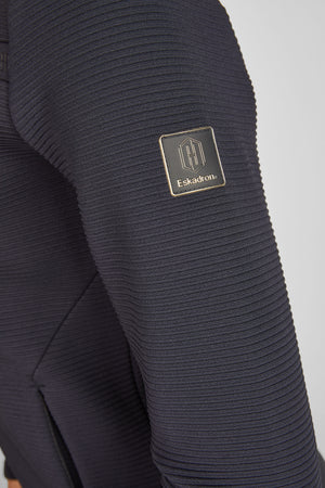 L'image montre un vêtement, plus précisément une manche d'un pull ou d'un haut. Le tissu présente une texture striée en relief, donnant un aspect légèrement texturé et tricoté. Le vêtement est de couleur bleu marine. Un élément notable de l'image est la présence d'un écusson brodé sur la partie supérieure de la manche. L'écusson est de forme carrée avec des coins arrondis et comporte une bordure dorée. À l'intérieur de l'écusson, il y a un logo stylisé composé d'un "H" et d'une sorte de...