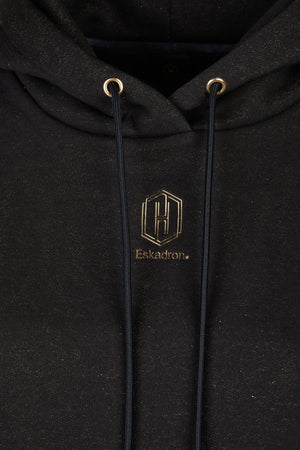 L'image présente un vêtement de type sweat-shirt à capuche de couleur noire. Le sweat-shirt est orné d'un logo doré positionné sur le côté gauche de la poitrine. Ce logo est composé d'un motif géométrique avec trois barres verticales entourées d'un cadre rectangulaire. Sous ce motif, le nom "Eskadron" est inscrit en lettres dorées. Le sweat-shirt possède une capuche avec des cordons de serrage noirs, traversant des œillets dorés. Le tissu semble légèrement brillant, ajoutant une touche...