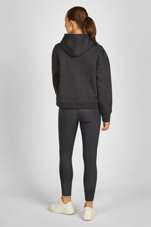 L'image montre une femme de dos, vêtue d'un ensemble de vêtements de sport. Elle porte un sweat-shirt gris foncé avec une capuche, dont les manches longues descendent jusqu'à ses poignets. Le sweat-shirt semble être en tissu molletonné et a une coupe légèrement ajustée. En dessous, elle porte un legging moulant noir qui descend jusqu'à ses chevilles. Les leggings ont une bande de tissu plus épaisse sur le côté extérieur des cuisses. Elle porte des chaussures de sport blanches avec une semelle...