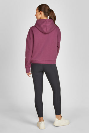 L'image montre une femme vue de dos. Elle porte une tenue décontractée, idéale pour une activité sportive ou un moment de détente. Voici une description plus détaillée : - **Vêtements** : - **Haut** : Elle porte un sweat-shirt à capuche de couleur bordeaux. Le sweat-shirt semble être en tissu molletonné, offrant ainsi confort et chaleur. Il a des manches longues et une capuche bien ajustée. - **Bas** : Elle est vêtue de leggings noirs moulants qui descendent jusqu'aux chevilles. Les...