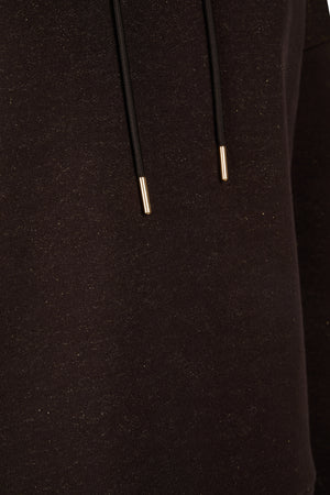 L'image présente une vue rapprochée d'un vêtement noir, probablement un sweat-shirt ou une veste à capuche. Le tissu semble être en jersey, avec une texture légèrement pelucheuse et douce. Il y a deux cordons de serrage visibles, chacun avec des embouts métalliques dorés. Ces cordons sont situés au niveau de la capuche, indiquant qu'ils servent à ajuster l'ouverture de la capuche. Le tissu présente de petites particules brillantes dispersées de manière aléatoire, lui donnant un aspect...