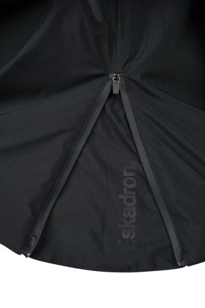 L'image montre la partie inférieure d'un parapluie noir, vue de dessous. Le tissu du parapluie est en nylon noir, structuré avec plusieurs sections triangulaires cousues ensemble. Une fermeture éclair, partiellement ouverte, est visible au centre de l'image, permettant de voir l'intérieur de l'une des sections. Le parapluie porte la marque "Eskadron", inscrite de manière discrète en lettres blanches sur l'une des sections du côté intérieur. Le tissu semble solide et résistant, typiquement...