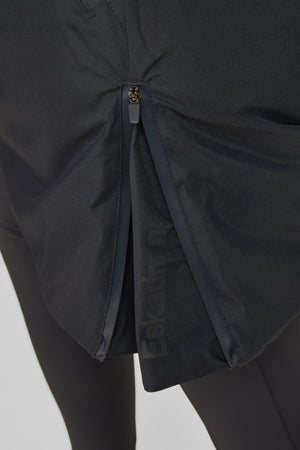 L'image montre une vue rapprochée de l'arrière d'un vêtement, probablement une veste ou un pantalon de sport, principalement de couleur noire. Le tissu semble être léger et respirant, idéal pour les activités sportives. Voici une description détaillée : 1. **Fermeture Éclair** : Il y a une fermeture éclair verticale centrale de couleur noire qui relie deux sections du tissu. La fermeture éclair a un curseur noir avec un petit logo ou une inscription dorée dessus. 2. **Tissu** : Le tissu...