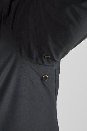 L'image montre une vue rapprochée de l'avant d'un vêtement, plus précisément une veste, de couleur noire. La veste présente deux boutons métalliques de couleur cuivrée, fixés verticalement sur le côté gauche. Ces boutons sont utilisés pour fermer la veste. Le tissu de la veste semble être texturé et de bonne qualité, avec un aspect légèrement mat. La partie intérieure de la veste, visible où le vêtement est ouvert, semble être doublée d'un tissu plus souple et plus lisse, également de couleur...