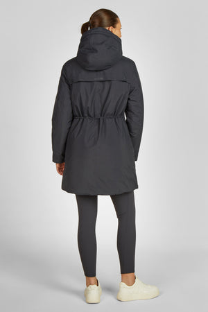 L'image montre une personne vue de dos, portant un ensemble de vêtements sportifs et fonctionnels. - **Manteau** : La personne porte un manteau couleur gris foncé. Ce manteau semble être conçu pour l'extérieur, probablement pour les activités sportives ou les conditions climatiques variables. Il possède une capuche pliable qui est actuellement relevée. Le manteau est cintré à la taille grâce à un cordon de serrage, ce qui lui donne une silhouette ajustée et élégante. - **Pantalon** : Le...