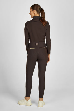 L'image présente une femme vue de dos, debout contre un fond blanc. Elle porte un ensemble de vêtements sportifs de couleur marron foncé, composé d'un haut à manches longues et d'un pantalon ajusté. Le haut est de coupe ajustée, avec un col montant et des manches longues qui s'arrêtent aux poignets. Le pantalon est également de coupe ajustée, avec des coutures apparentes et deux poches latérales visibles, chacune ornée d'une fermeture éclair dorée. La femme a les cheveux attachés en une...