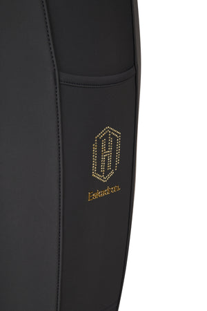 L'image présente un gros plan sur une partie d'un pantalon noir. Ce pantalon semble être conçu pour l'équitation ou pour des activités sportives, étant donné sa coupe ajustée et les matériaux utilisés. Sur le côté du pantalon, il y a une couture verticale qui sépare deux sections différentes du tissu. La section principale, à gauche de la couture, est faite d'un tissu noir mat, probablement en polyester ou en un autre matériau synthétique, offrant une apparence lisse et moderne. À droite de...