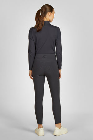 L'image montre une femme vue de dos, portant une tenue de sport noire. Elle est composée d'un haut à manches longues avec un col montant et d'un pantalon moulant qui s'arrête juste au-dessus des chevilles. Le haut a une coupe ajustée et semble être en matière stretch, probablement conçu pour offrir une bonne liberté de mouvement. Il est noir uni et présente un petit logo ou motif discret au niveau des omoplates. Le pantalon est également noir et présente un motif texturé subtil sur les...