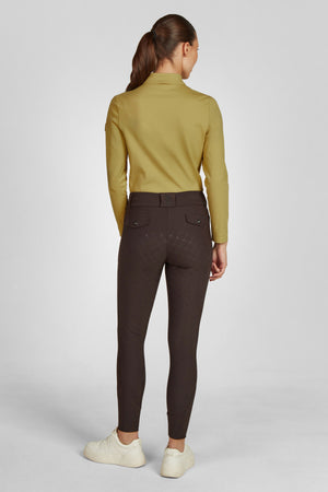 Sur cette image, on voit une personne de dos, se tenant debout avec les mains le long du corps. Elle porte une tenue composée de deux pièces : 1. **Haut** : Un chemisier à manches longues de couleur moutarde. Le tissu semble lisse et ajusté, mettant en valeur la forme du haut du corps. La coupe est classique avec un col montant et des manches longues qui s'arrêtent aux poignets. 2. **Bas** : Un pantalon ou un legging en tissu brun foncé. Le vêtement est ajusté, épousant les formes des...