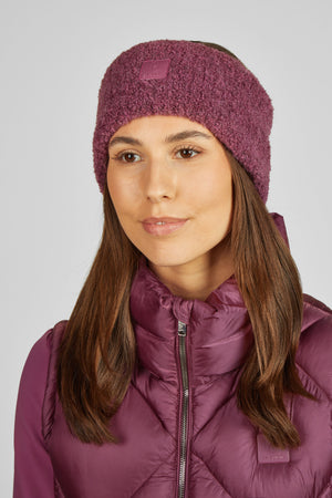 L'image représente une femme portant une tenue d'hiver dans un style violet harmonieux. Elle porte un bonnet tricoté violet, doux et moelleux, qui semble être en matière polaire. Le bonnet est orné d'un petit patch rectangulaire sur le côté, avec un logo ou une marque. Elle est également vêtue d'une veste matelassée violette, probablement en tissu isolant, ce qui suggère qu'elle est conçue pour fournir chaleur et confort. La veste a une fermeture éclair centrale et une coupe ajustée, avec...